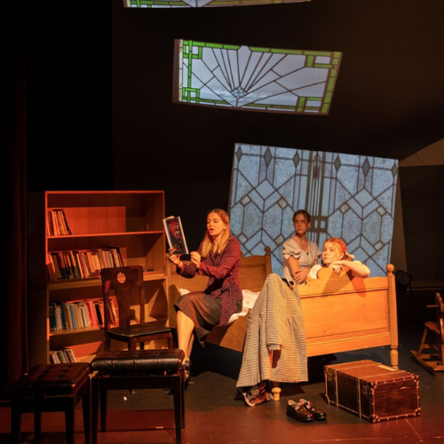 three actresses on stage with bookshelves, bed and stained glass windows