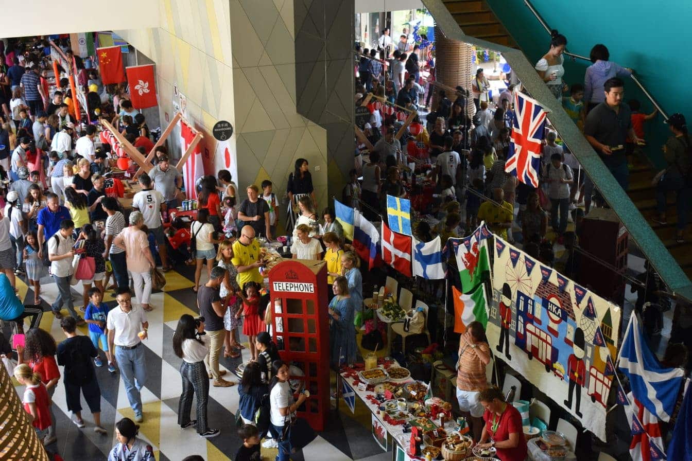 Families and students celebrating cultural diversity at a Hong Kong Academy community event featuring international flags and food stalls in our Sai Kung campus atrium.